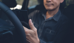 man seated at steering wheel using dealer locator app on mobile device to find nearby contractor